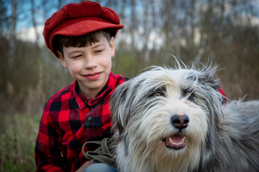 A cheerful boy in a red hat with a bearded collie dog smiling outdoors.